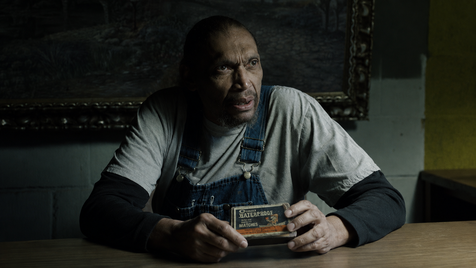 An old man in overalls holding a vintage box of waterproof safety matches